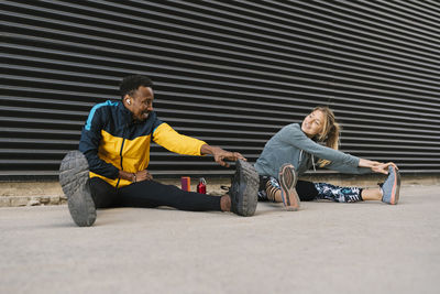 Male and female sportsperson doing stretching exercise while sitting on floor against back wall