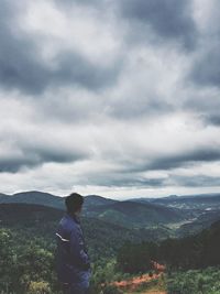 Rear view of man standing on mountain against sky