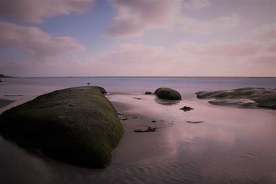 Rocks on beach against sky during sunset