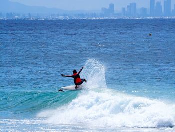 Rear view of man with arms outstretched surfing in sea