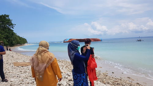 Rear view of people on beach against sky