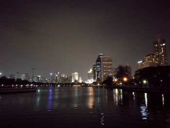 Illuminated city by river against sky at night