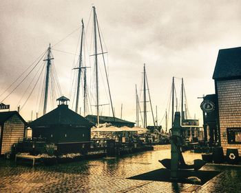 Sailboats moored at harbor by buildings against sky