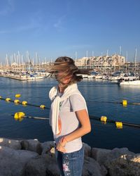 Woman tossing hair standing on rock by sea against sky