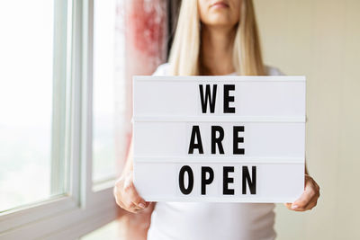 Midsection of woman holding open sign at cafe