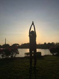 Silhouette man standing at riverbank against sky during sunset