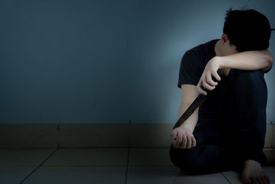 Young woman sitting on floor against wall