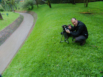 Full length portrait of man photographing while crouching on grass