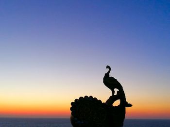 Silhouette statue on beach against clear sky during sunset