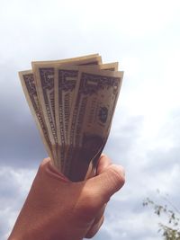 Close-up of hand holding paper against the sky