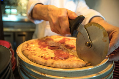 Midsection of chef cutting pizza at restaurant