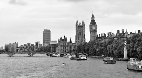 Big ben in city by river against cloudy sky