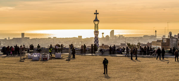 People standing by cross against sky during sunset in city