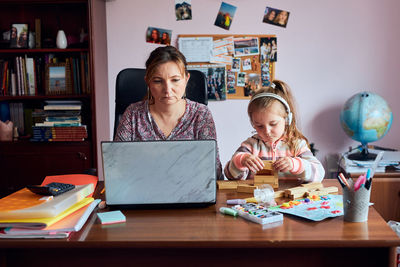 Mother working in laptop while daughter playing with cube shape on table at home