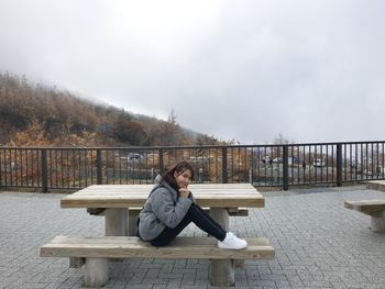 Portrait of woman sitting on bench against sky