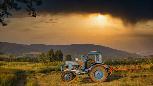 Tractor on field against sky during sunset