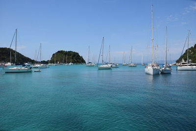 Sailboats moored on sea against blue sky