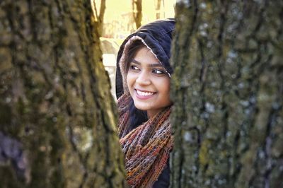 Smiling young woman seen through tree trunk