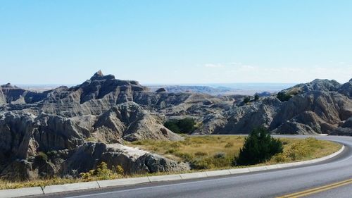 Empty road along rocky mountains against clear blue sky