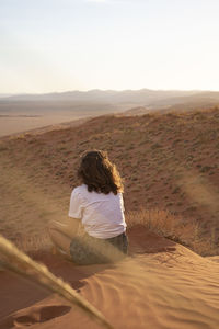 Rear view of woman sitting on sand