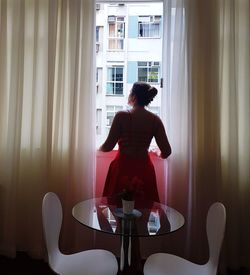 Rear view of woman standing on chair at home