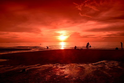 Silhouette people on beach against orange sky