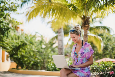 Young woman using phone while sitting on tree