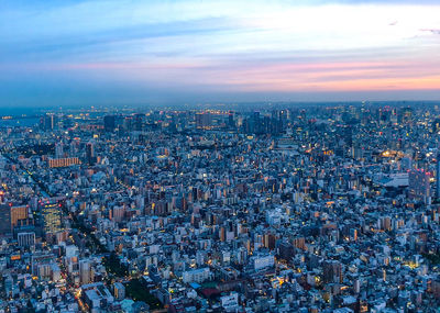 High angle view of illuminated city buildings against sky at sunset