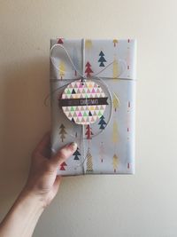 Cropped image of woman hand holding christmas present against wall