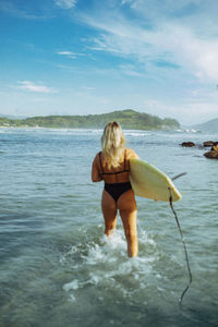 Rear view of woman in bikini standing in sea against sky