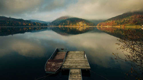 Boat moored by jetty on lake against cloudy sky