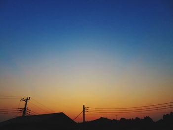 Silhouette electricity pylons against clear sky during sunset