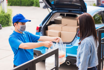 Delivery person wearing mask giving food to client outdoors