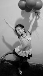 Cheerful girl holding balloons against wall