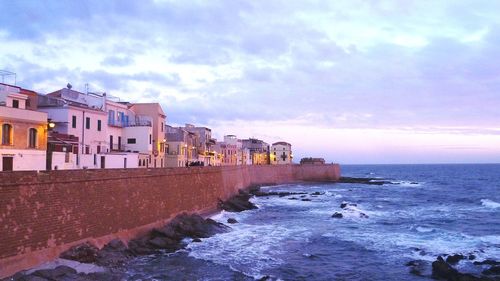 Buildings by sea against sky during sunset