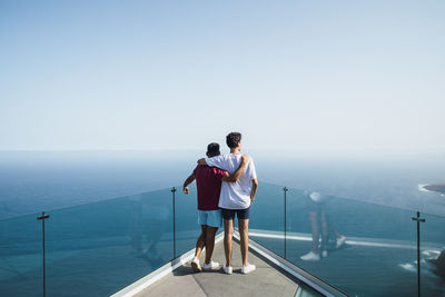 Young friends with arms around looking at sea from mirador del balcon, grand canary, canary islands, spain
