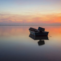 Boat floating on sea against sky during sunset