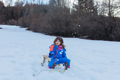 Portrait of smiling boy sitting on snow covered field