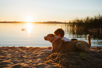 People relaxing on beach against sky during sunset