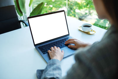 Mockup image of a woman using and typing on laptop keyboard with blank white desktop screen