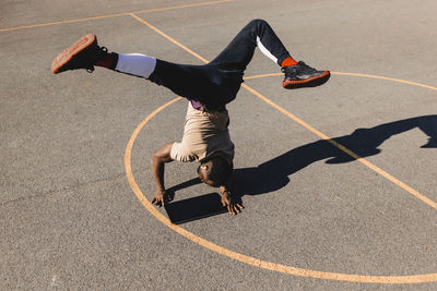 Young man balancing with handstand using graphics tablet on basketball court during sunny day