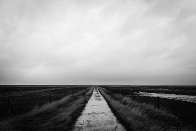 Empty road amidst field against sky