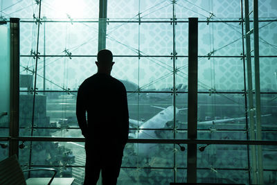 Rear view of silhouette man standing by window