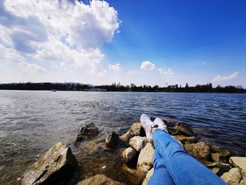 Low section of person by lake against sky