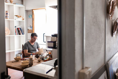 Man sitting at table with brushes and drawing sketches on handmade ceramic plate