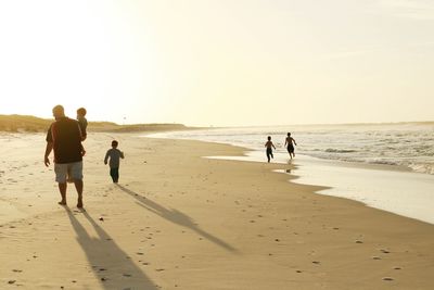 Full length rear view of father with sons at beach against sky