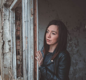 Woman looking away standing by door of abandoned building 