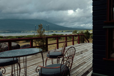 Empty chairs and table by sea against sky