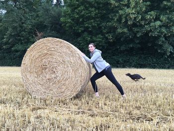 Portrait of woman pushing hay bale on field