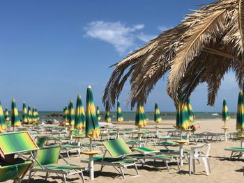 Empty chairs and tables on beach against sky